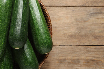 Raw ripe zucchinis in wicker basket on wooden table, top view. Space for text