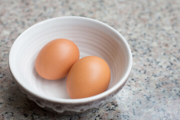 Two fresh light brown eggs in a cup on a granite table.