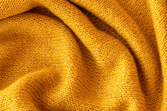 Soft knitted yellow sweater texture closeup. Light orange abstract background. Trendy soft mustard-colored backdrop for web design. Luxury twisted fabric backplate 