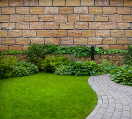 Obraz premium Garden stone path with grass growing between the stones against the backdrop of a stone wall.