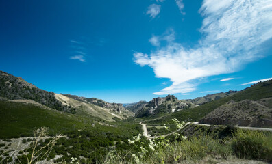 Road to the mountain with snow under the blue sky with grass fields and steppes. Valley in nature, angular view of the environment.	
