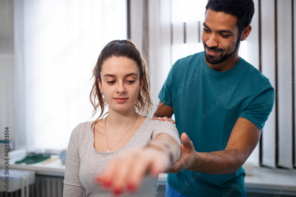 Wall mural Young male physiotherapist examining young woman patient in a physic room