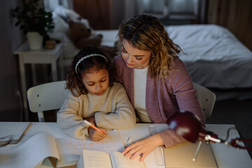High angle view of little girl doing homework with her mother in evening at home.