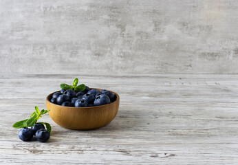 Blueberries in a wooden bowl with a sprig of mint on a light wooden table. Fresh large berries on the table. Light wooden background. Space for text