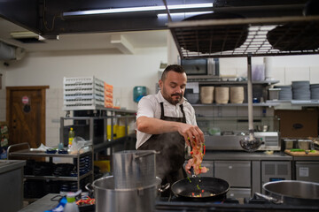 Fototapeta na wymiar Mature chef adding chopped vehetagles to pan indoors in restaurant kitchen.