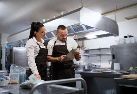 Chef and cook discussing menu indoors in restaurant kitchen.
