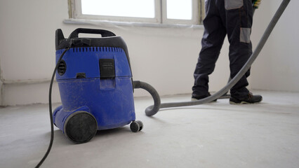 Worker washes the floor with a vacuum cleaner from industrial concrete dust and cement mud during...