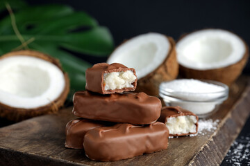 Delicious milk chocolate candy bars with coconut filling on wooden board, closeup