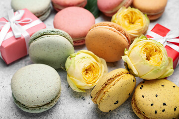 Sweet macaroons and beautiful rose flowers on light background, closeup