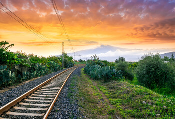 old evening railroad leading to a sunset glow in mountains with green bushes and cjlorful cloudy...