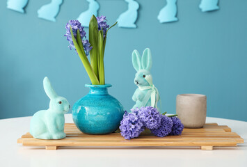 Vase with beautiful hyacinth flowers and Easter bunnies on table against blue background