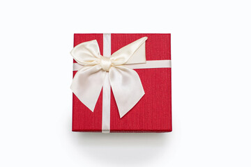 Red gift box with a white ribbon and a bow on a white paper background. Gift for birthday or traditional holiday. Gift box close up