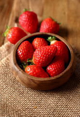 Strawberries placed in a wooden bowl on a wooden floor