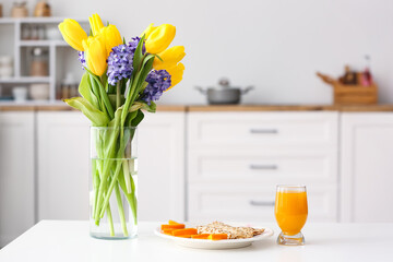 Vase with flowers and tasty breakfast on dining table in kitchen