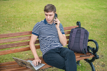 Young caucasian man sitting on the bench, working on the laptop and making
