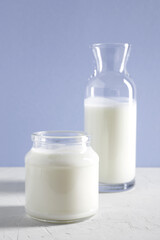 Yogurt, kefir or fermented milk product in glasses jar and bottle on a white table. White-lilac background. Healthy food concept