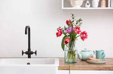 Vase with flowers and breakfast on kitchen counter near white wall