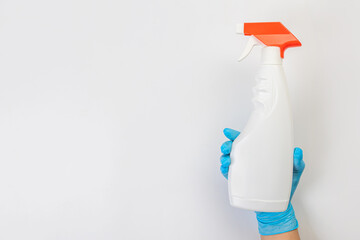 The hand of a cleaning lady in a blue rubber glove holds a bottle of cleaning agent on a gray background. Detergent for various surfaces in the kitchen, bathroom and other rooms. Close-up.