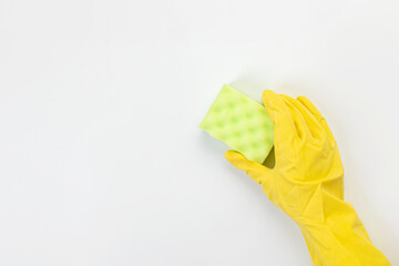 The hand of a housewife in a yellow protective rubber glove holds a sponge for cleaning agent on a gray background. Detergent for various surfaces in the kitchen, bathroom and other rooms. Close-up.