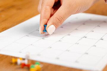 Blue Hand pin stuck on the day of the month in the calendar, business concept. beautiful female hand fingers