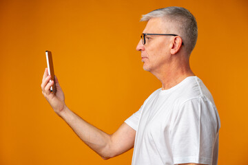Senior smiling man using smartphone over yellow background