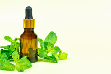 Essential oil of fragrant mint (peppermint) in a brown bottle with a pipette on a bright yellow background. Aromatherapy, spa, skin care. Space for text.