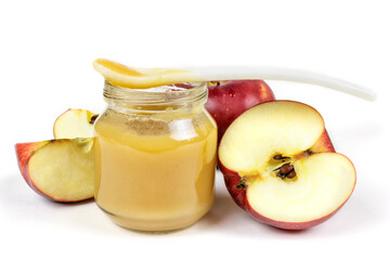 Baby food. A glass jar with baby apple puree with a spoon and slices of red juicy apple on a white isolated background. The first fruit lure of the baby.