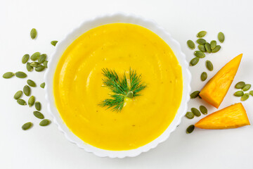 Pumpkin soup puree in a beautiful plate with dill, pumpkin seeds and pieces close-up on a white background.