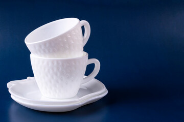 Two beautiful white cups (mugs) in the shape of strawberries and two saucers are stacked on top of each other on a dark blue background. Empty clean dishes. Space for text.