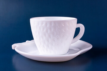 A beautiful white cup (mug) in the shape of a strawberry stands on a saucer on a dark blue background. Empty clean dishes.