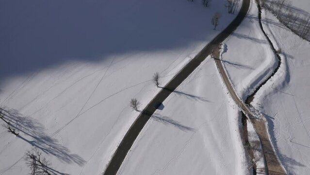 Blue van wheeling along an empty asphalt road in a snowy country field, aerial view.