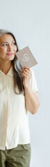 Thoughtful hoary haired Asian lady customer holds gift card standing on light grey background in studio. Shopping certificate