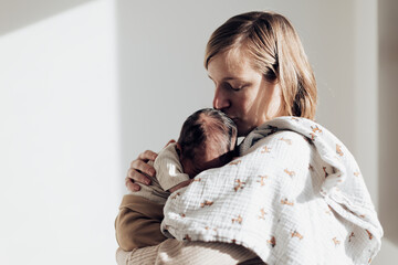 mom holds her little newborn baby in her arms sleeping with her face in her chest - sunlight in the room - Powered by Adobe