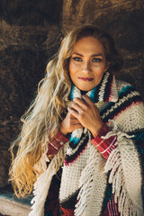 Mature woman enjoys a winter day in a stone cabin with her traditional Mexican poncho (Quechquemitl) next to a wall by the fireplace.