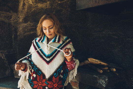 Mature woman enjoys a winter day in a stone cabin with her traditional Mexican poncho (Quechquemitl) next to a wall by the fireplace.