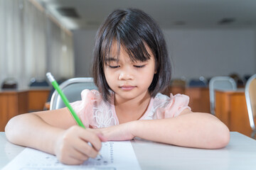 A female Asian kid student concentrate writing on the examination paper in the class