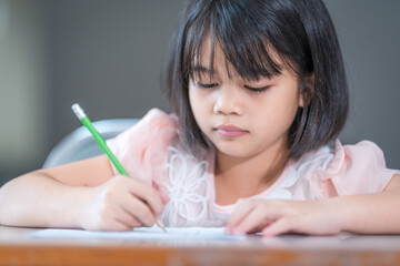 A female Asian kid student concentrate writing on the examination paper in the class