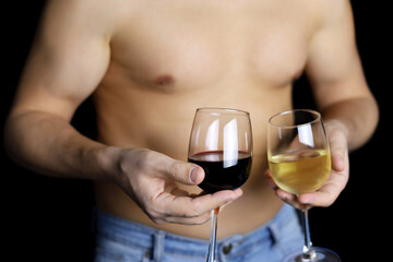 Muscular man in with naked torso standing with glasses of red and white wine in hands on black background. Concept of choosing alcohol drink, romantic date