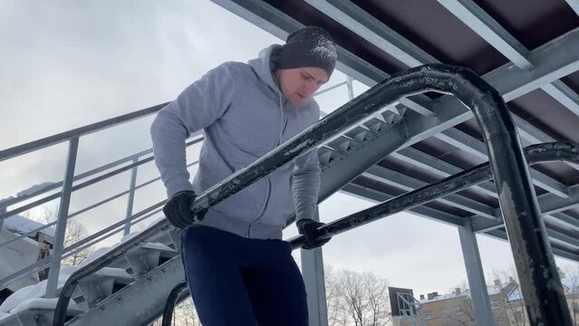 Young athletic man doing dips on a parallel bars during his outdoor winter workout