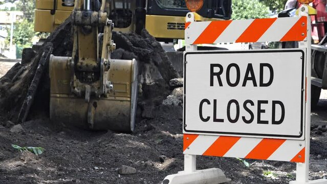 Road construction site machine is digging in slow motion  with a road closed sign