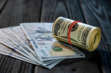 A roll of dollar bills and coins over other bills on a desk