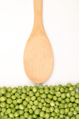 Green peas and an empty bamboo spoon on a white background.Gastronomy, cooking and recipes of pea dishes, vegetarianism, protein production, sports nutrition.Vertical photo