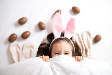 Happy Easter. cute beautiful girl with blue eyes and bunny ears peeking out from under the blanket....