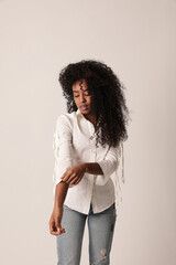 Confident young black woman posing on grey wall, looking at the camera.