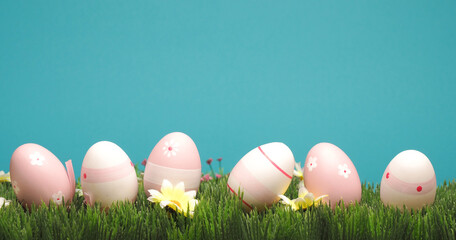 Pink Easter eggs in a row on grass with flowers