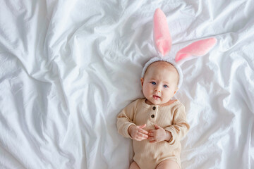 Dressed up for Easter. A cute funny baby with bunny ears costume dressed up for Easter laying on white bed linen sheet.