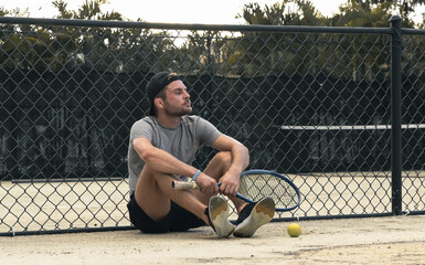 Man tennis player sitting on the tennis court and waiting his turn for playing tennis.
