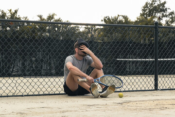Tired tennis player sits on the court, losses in sports , failure emotions of sportsman.