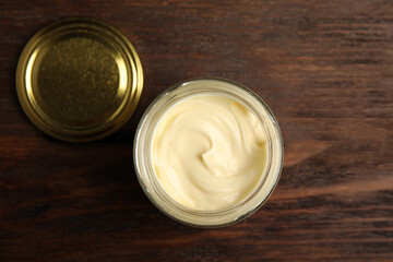 Jar of delicious mayonnaise and lid on wooden table, flat lay