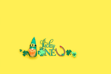 "Lucky one" text, cute irish gnome, horseshoe, clover leaves on bright yellow background. symbol of 17 march, Saint Patrick day, traditional irish holiday. flat lay